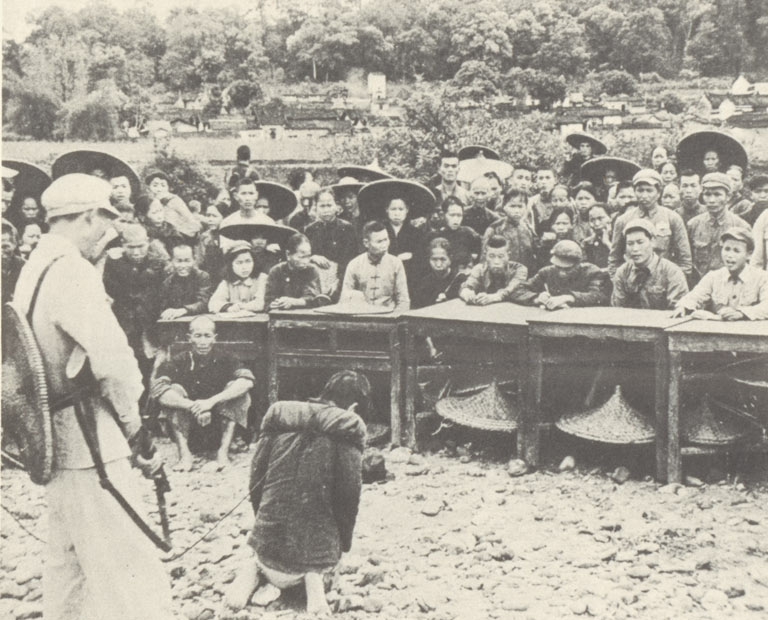 A village landowner bound on his knees before armed peasant militia and assembled villagers during a public land reform struggle tribunal.